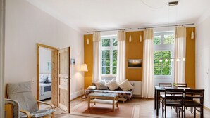 Une pièce comprenant un canapé, une table à manger avec des chaises, une lampe et une fenêtre avec des rideaux.