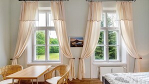 Une pièce comprenant un lit, une table, deux chaises et deux fenêtres avec des rideaux.
