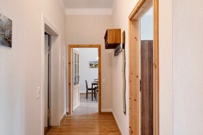 A hallway with wooden flooring, white walls, and a dining area in the background.