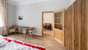 Ein Zimmer mit einem Bett, einem Esstisch mit Stühlen, einem Holzschrank und Blick in einen weiteren Raum.