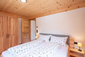 A wooden ceiling, a bed with floral bedding, a bedside lamp, and wooden wardrobes.