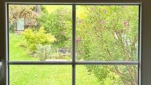 A window with a view of a garden, a stone wall, and a tree with purple flowers. - Apartment 'Fuldawiesen' with Balcony and Wi-Fi (Schlitz)
