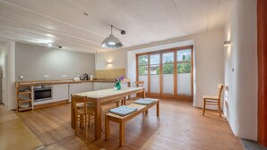 Een ruime keuken met houten vloeren, een eethoek met een tafel en banken, en een groot raam met uitzicht op groen.