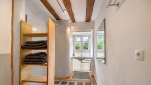 Een smalle gang met een houten plank waarop handdoeken, een wastafel en een spiegel aan de rechterwand staan.
