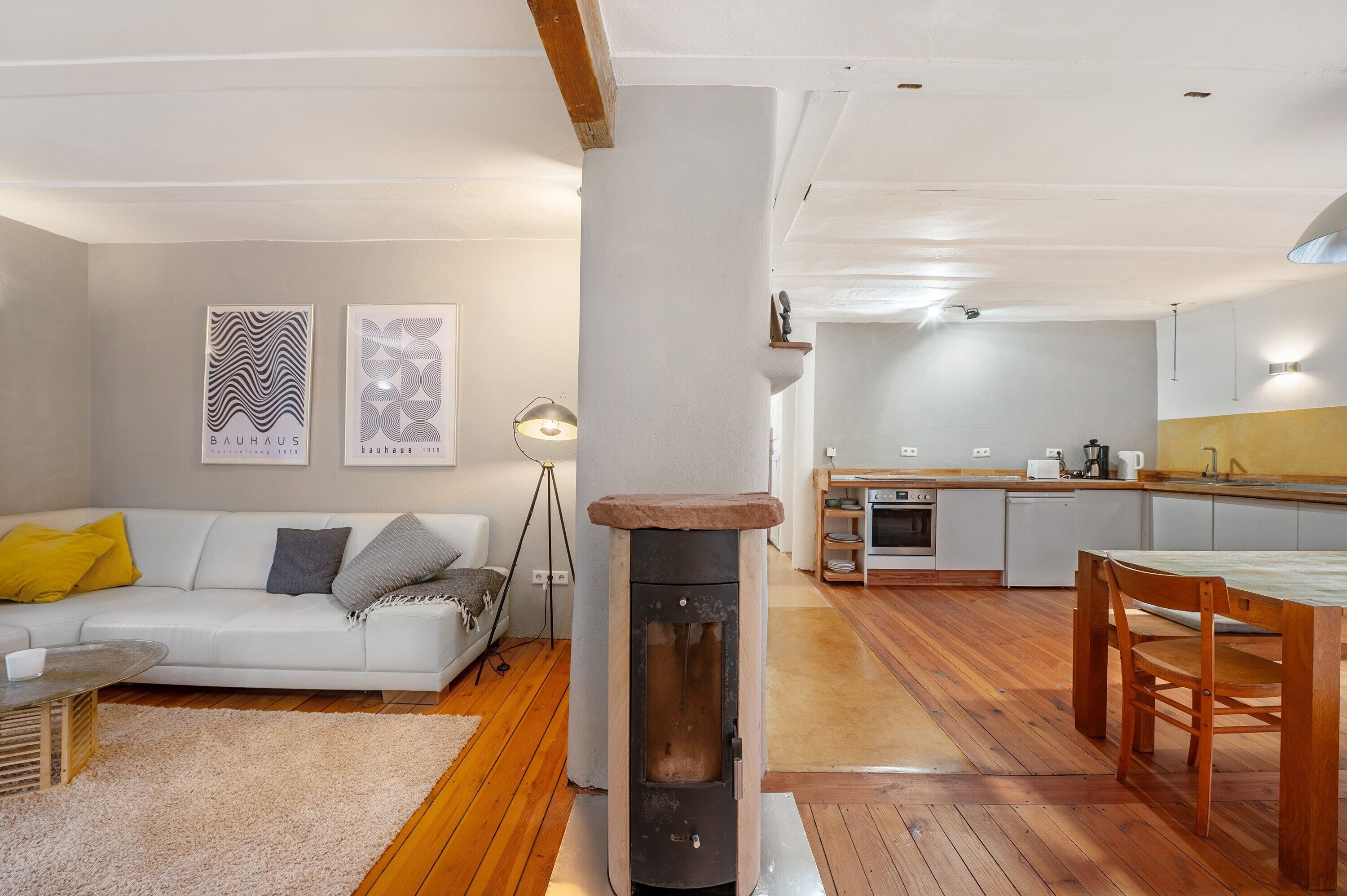 A modern living room with a sofa, a table, and a fireplace. There is a kitchen area with a dining table and chairs.