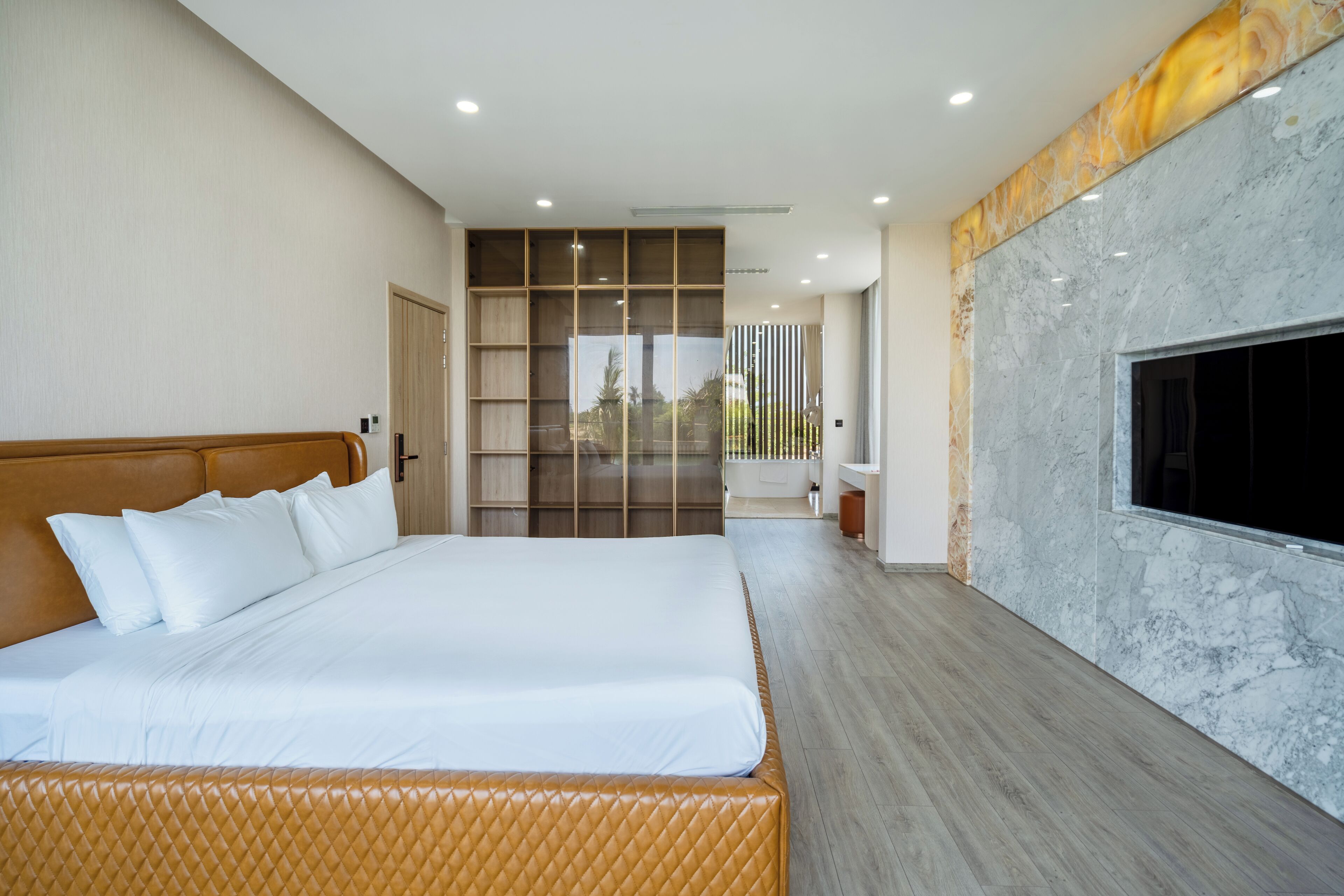 A modern hotel room with a large bed, a built-in wardrobe, a marble accent wall, and a view of the outside.