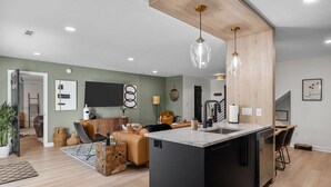 A modern kitchen with a central island, a dining area with chairs, and a living room with a sofa and a coffee table. - Modern 7BR Triplex | Sleeps 20 | Steps to Beach (North Myrtle Beach)