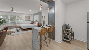 A modern kitchen with a central island, bar stools, and a cart with kitchenware. - Modern 7BR Triplex | Sleeps 20 | Steps to Beach (North Myrtle Beach)