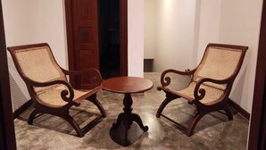 Quarto com duas cadeiras de madeira com assentos trançados e uma pequena mesa redonda.