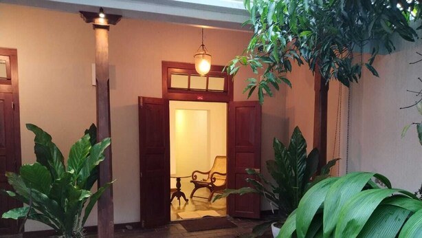 Uma entrada tradicional com porta de madeira, um banco no interior e plantas em vasos ao redor.