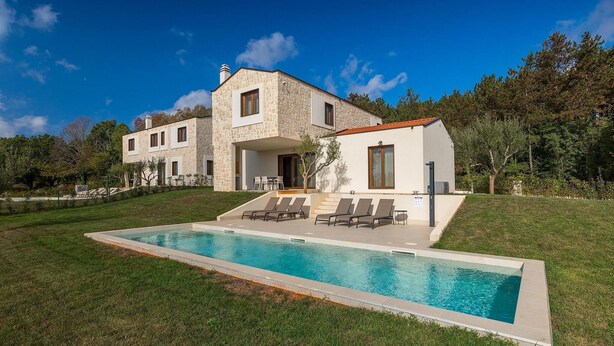 Une maison moderne à deux étages, dotée d’une façade en pierre, d’une piscine avec des chaises longues et d’une pelouse bien entretenue.