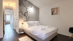 Une chambre à coucher comprenant un lit, une table de chevet, une lampe, un tableau et une porte donnant sur une autre pièce.