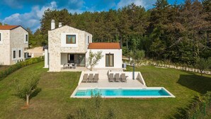 Une maison en pierre avec une piscine, une terrasse avec des chaises et un paysage boisé en arrière-plan.