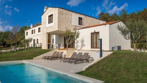 Une maison moderne à deux étages, dotée d’une façade en pierre, d’une piscine et d’un espace de détente extérieur.