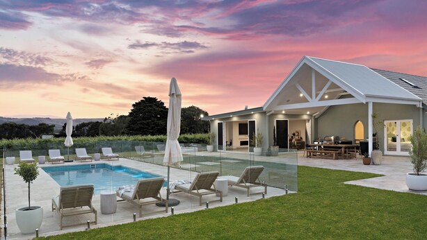 Una casa moderna con piscina, mobiliario de exterior y un porche cubierto.