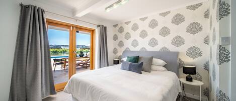 A bedroom with a large bed, a nightstand, a lamp, and a view of a pool and outdoor area.