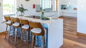 Una cocina moderna con armarios blancos, una isla central con taburetes, vigas de madera en el techo y un ventanal grande.