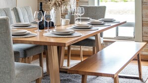 Comedor con mesa de madera dispuesta para seis personas, sillas grises tapizadas y un ventanal con vista arqueada.