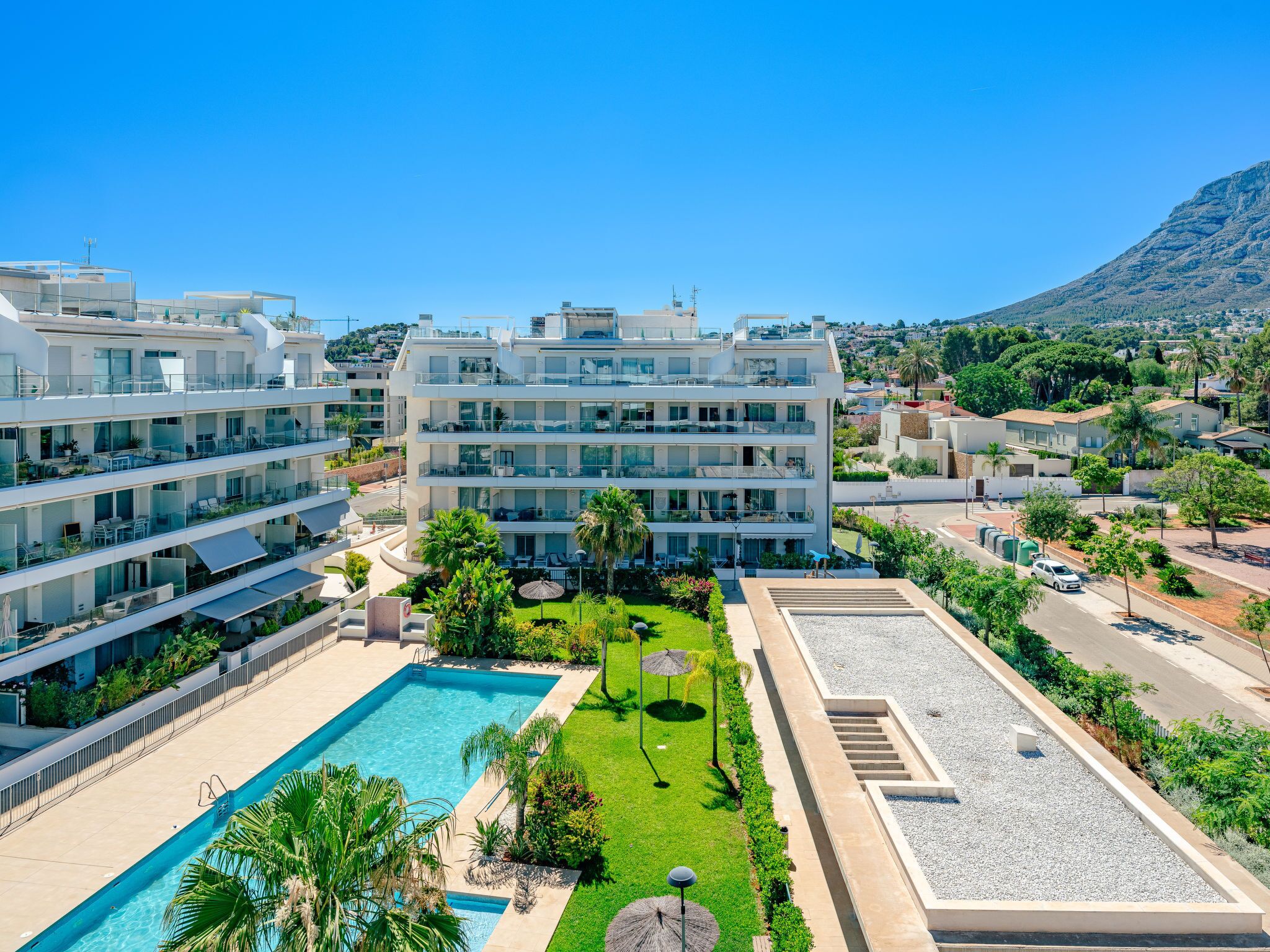 A modern hotel with multiple balconies, a swimming pool, and a landscaped garden.