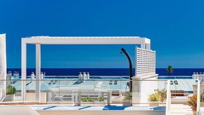 Eine Dachterrasse mit weißem Pergola, einem Pool und freiem Blick auf den Ozean.