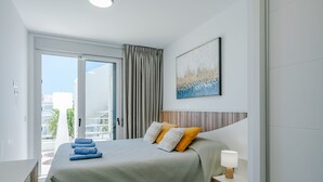Ein modernes Hotelzimmer mit einem großen Bett, einem Holzkopfteil, einem Nachttisch mit Lampe und Blick ins Freie durch eine Glastür.