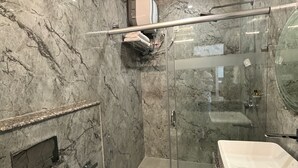 A bathroom with a marble wall, a glass shower enclosure, and a sink with a marble countertop. - Hotel white inn (Haldwani)