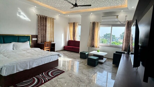 A modern hotel room with a marble floor, a large bed, a red sofa, a TV, and a ceiling fan. - Hotel white inn (Haldwani)