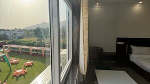 A hotel room with a large window, a bed, a small table, and a view of an outdoor area with tables and chairs. - Hotel white inn (Haldwani)
