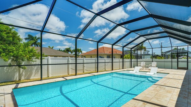 An indoor swimming pool with clear blue water, surrounded by a glass enclosure, and a view of the neighborhood. - 6 Mi to Beach: Cape Coral Home w/ Screened Lanai (Cape Coral)
