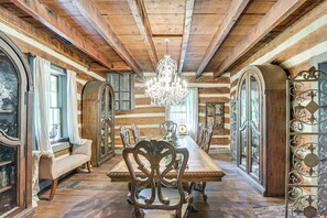 A log cabin interior with a wooden dining table, ornate chairs, a chandelier, and large windows with curtains. - Spacious & Historic Cabin in New Haven w/ Pond! (New Haven)
