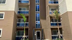 A multi-story building with balconies, a central entrance, and small trees in the foreground. - heavenly stay, three bedroom apartment w/pool (Santiago de los Caballeros)
