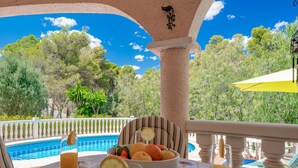Una mesa con un cuenco de fruta y vasos de zumo de naranja, con vistas a una piscina y abundante vegetación.