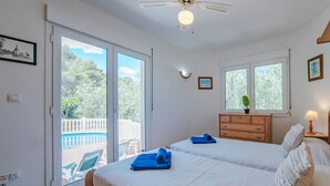 Un dormitorio con dos camas, ventilador de techo y vistas a una piscina y árboles a través de puertas corredizas de vidrio.