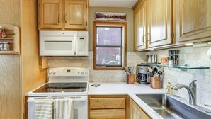 Una cocina con armarios de madera, una estufa blanca, un microondas y un ventanal con vista a un edificio de ladrillo.