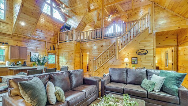 A spacious cabin interior with a wooden interior, a staircase, leather sofas, and a dining area. - 'Shady Pines' Mountain Retreat w/ Hot Tub! (Sevierville)