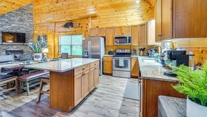 A spacious kitchen with wooden cabinets, a stone wall, and a large island with seating. - 'Shady Pines' Mountain Retreat w/ Hot Tub! (Sevierville)