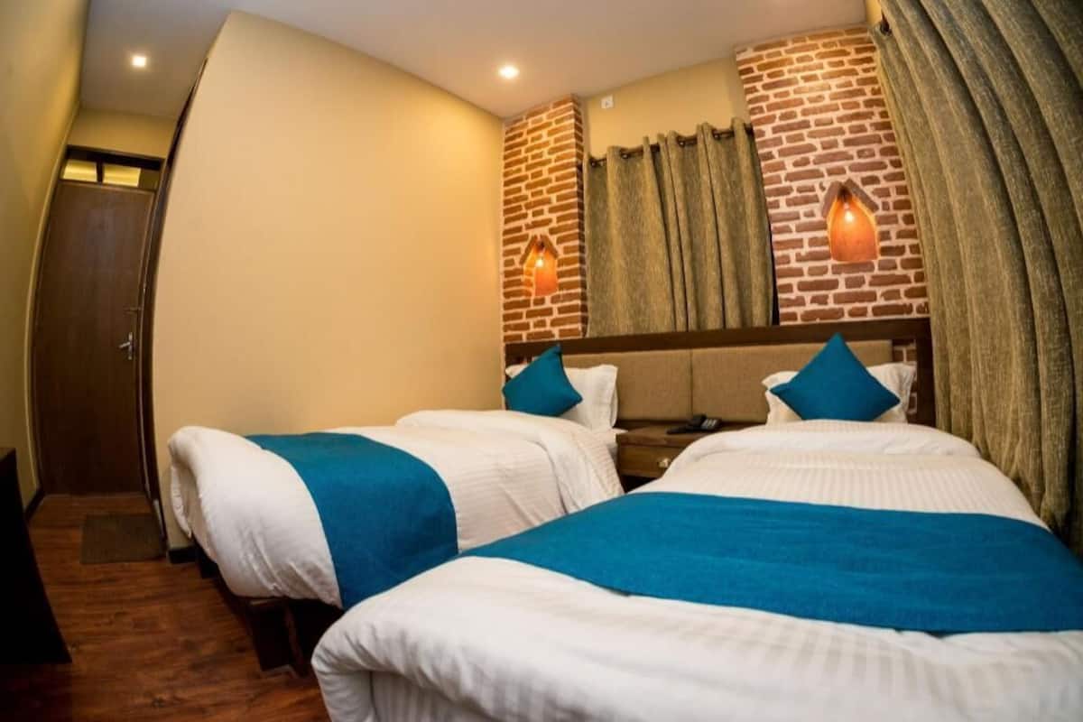 Quarto de hotel com duas camas, uma parede de tijolos e uma porta de madeira.