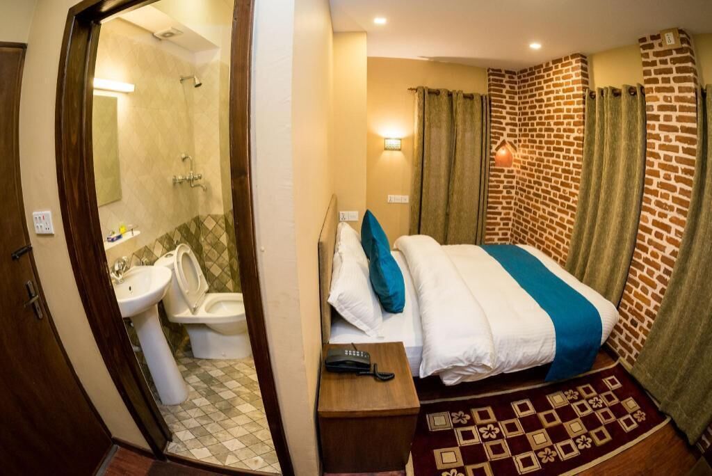 Une chambre d’hôtel comprenant un lit, une table de chevet avec un téléphone, une salle de bain avec des toilettes et un lavabo, ainsi qu’une douche.