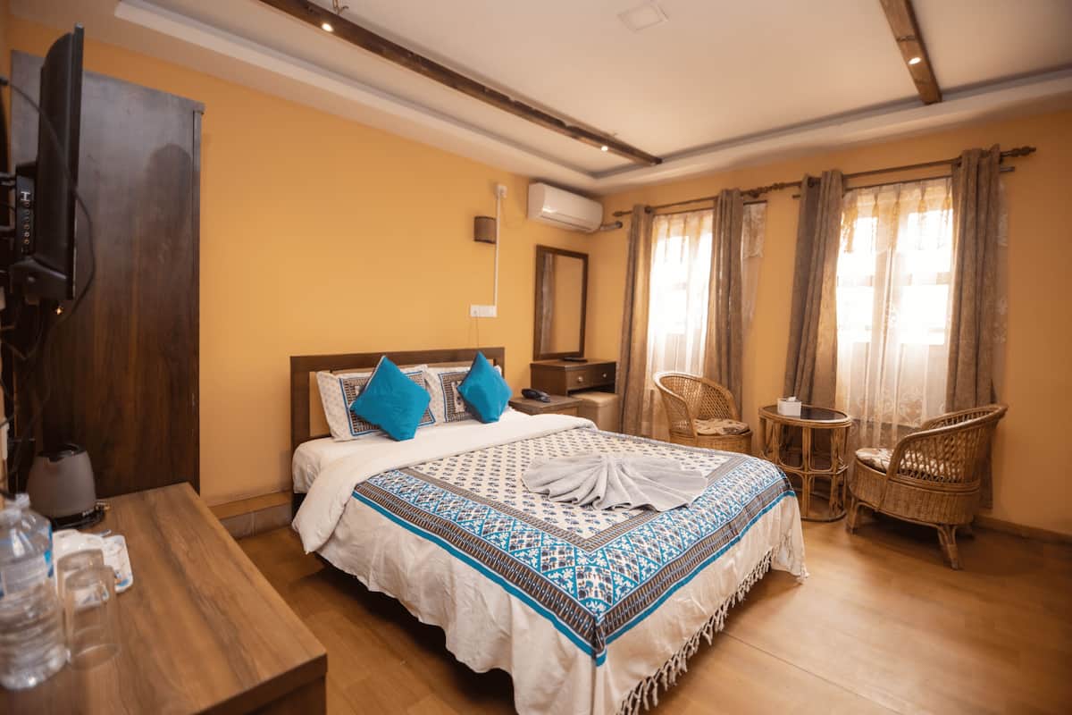 Quarto de hotel com cama, mesa de cabeceira de madeira, cadeira de vime, uma pequena mesa e televisão.