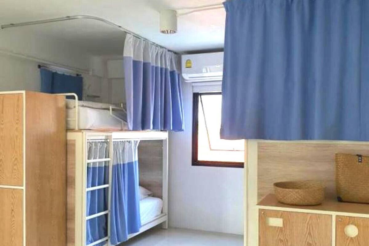 A compact room with bunk beds, a small cabinet, and a window with curtains.