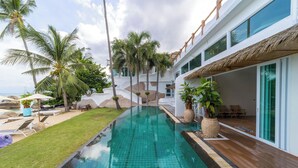 Una piscina con cubierta de madera, palmeras y sillas de descanso.