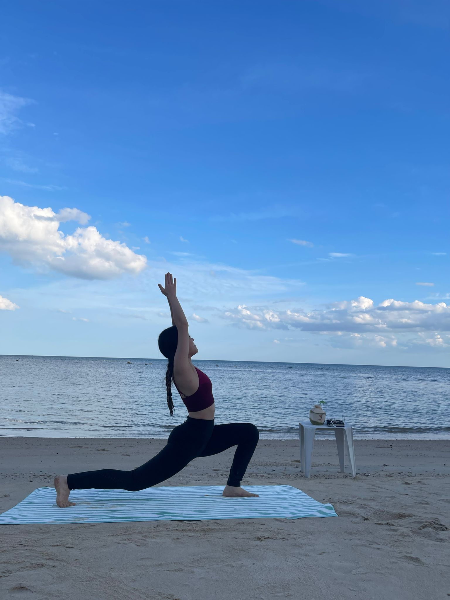 Una persona realizando una postura de yoga en la playa, con un cielo despejado y un mar tranquilo al fondo.