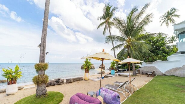 Un área de descanso en la playa con sillones, una mesita y un sillón de peluche morado.