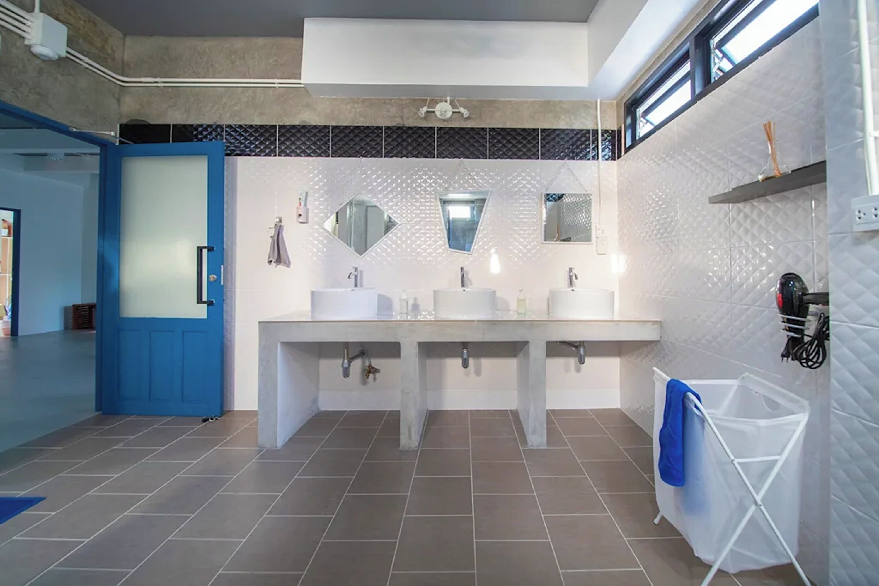A modern bathroom with two sinks, a blue door, and a white tiled wall with a diamond pattern.