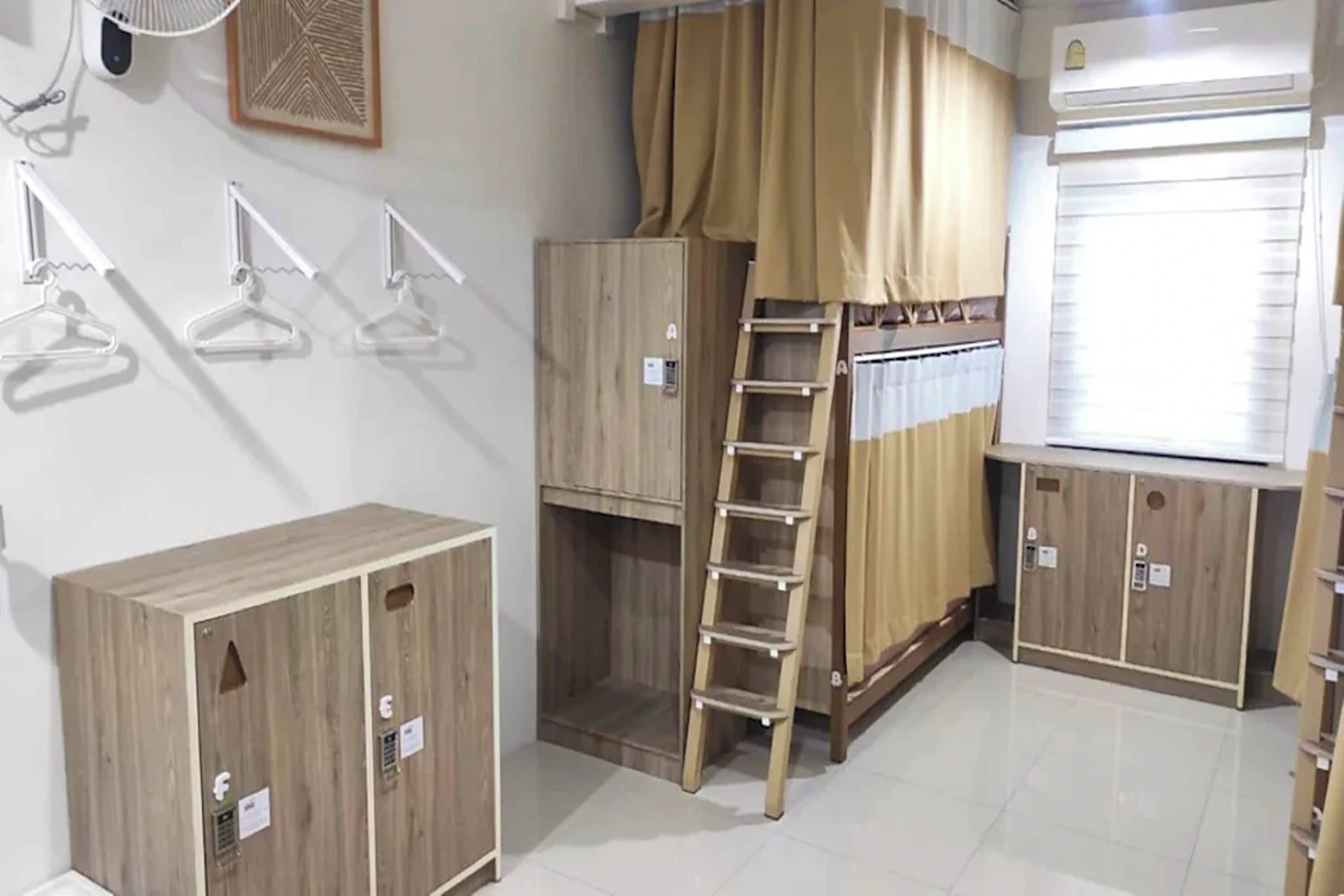 Une pièce avec un lit superposé, des armoires en bois, une échelle et une fenêtre avec des rideaux.