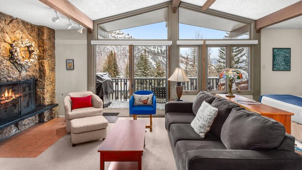 A cozy living room with a fireplace, comfortable seating, and large windows offering a mountain view. - Snowmass Condo W/ HT & Pool! Washer/Dryer, Balcony W/Grill, Wood FP & Covered Parking. (Snowmass Village)
