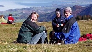 Un grupo de personas sentadas en una colina cubierta de hierba, con un paisaje montañoso al fondo.