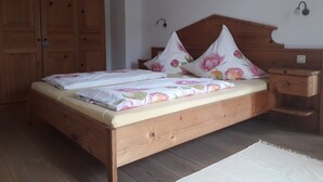 Una cama de madera con ropa de cama floral, una mesita de noche y un armario en una habitación con suelo de madera.