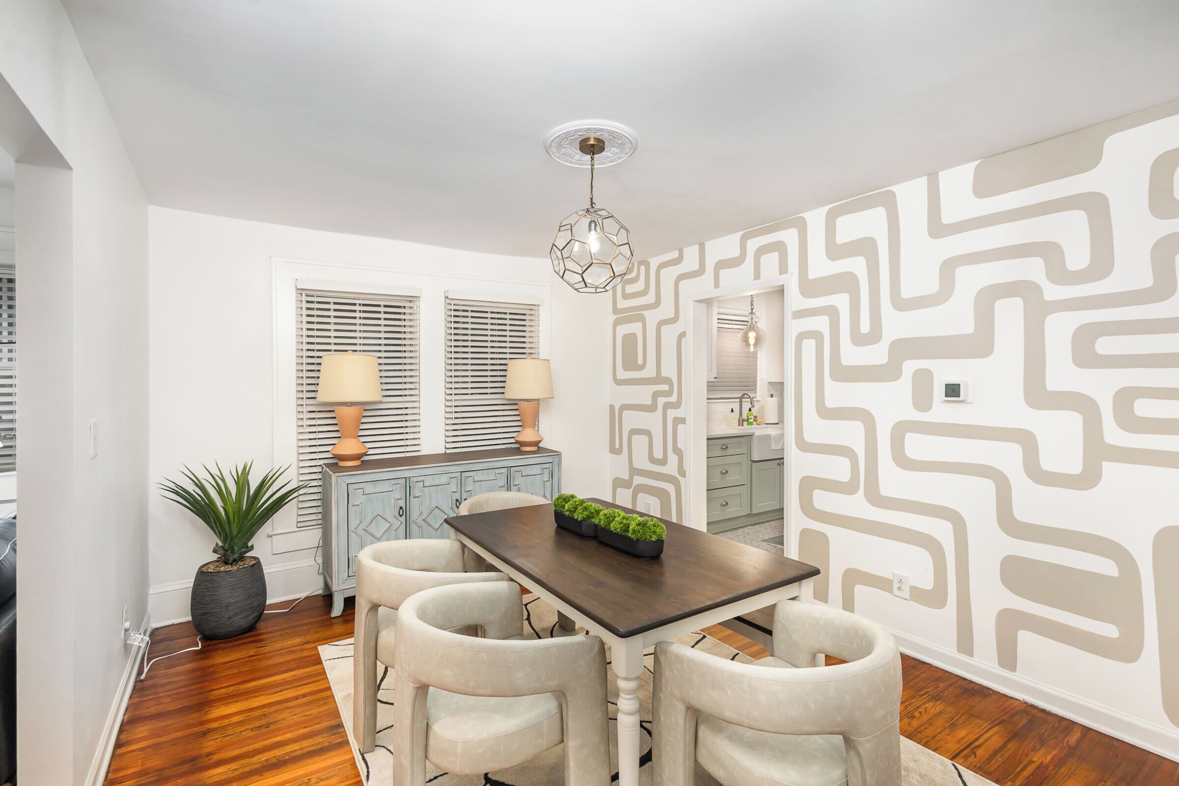 A dining area with a dark wooden table, four chairs, a potted plant, and a decorative wall with a geometric pattern.