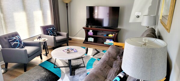 Una sala de estar con sofá, sillón, mesa de centro, televisor y lámpara.